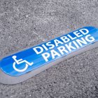 Com'Park ground marker laid flat on asphalt, blue visual with wheelchair symbol reading DISABLED PARKING