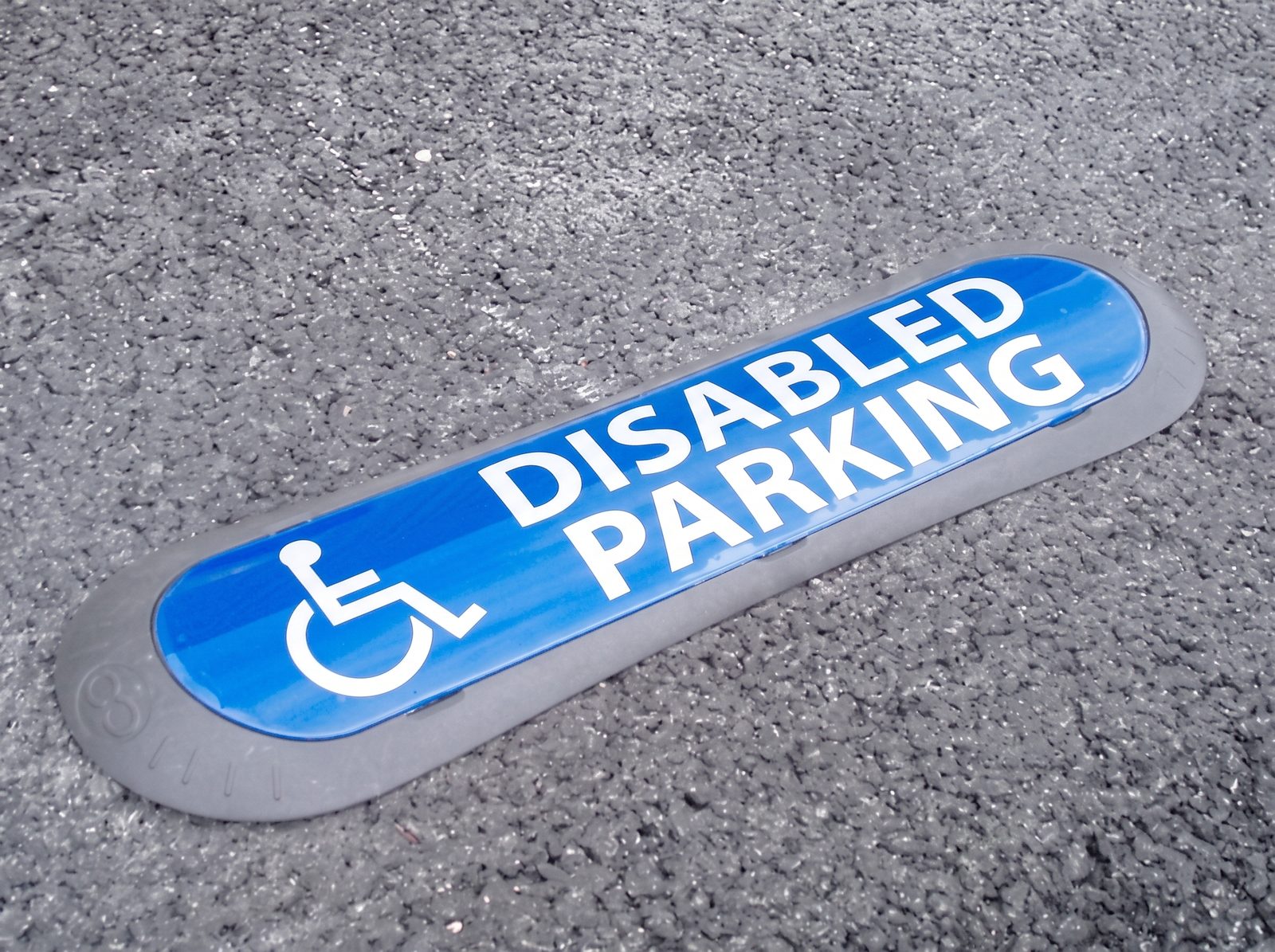 Com'Park ground marker laid flat on asphalt, blue visual with wheelchair symbol reading DISABLED PARKING